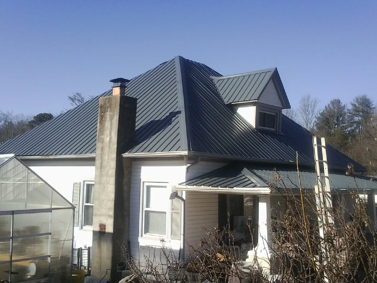 Dark blue standing seam metal roof on a white farmhouse with dormer — Slate & Tile Roof Repair by Roofing Brothers in Churchville