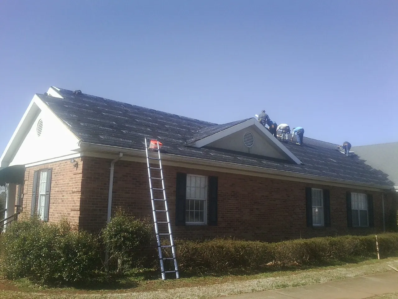 Crew tearing shingles off a brick ranch roof with a ladder set — Emergency Roof Repair work by our crew in Churchville